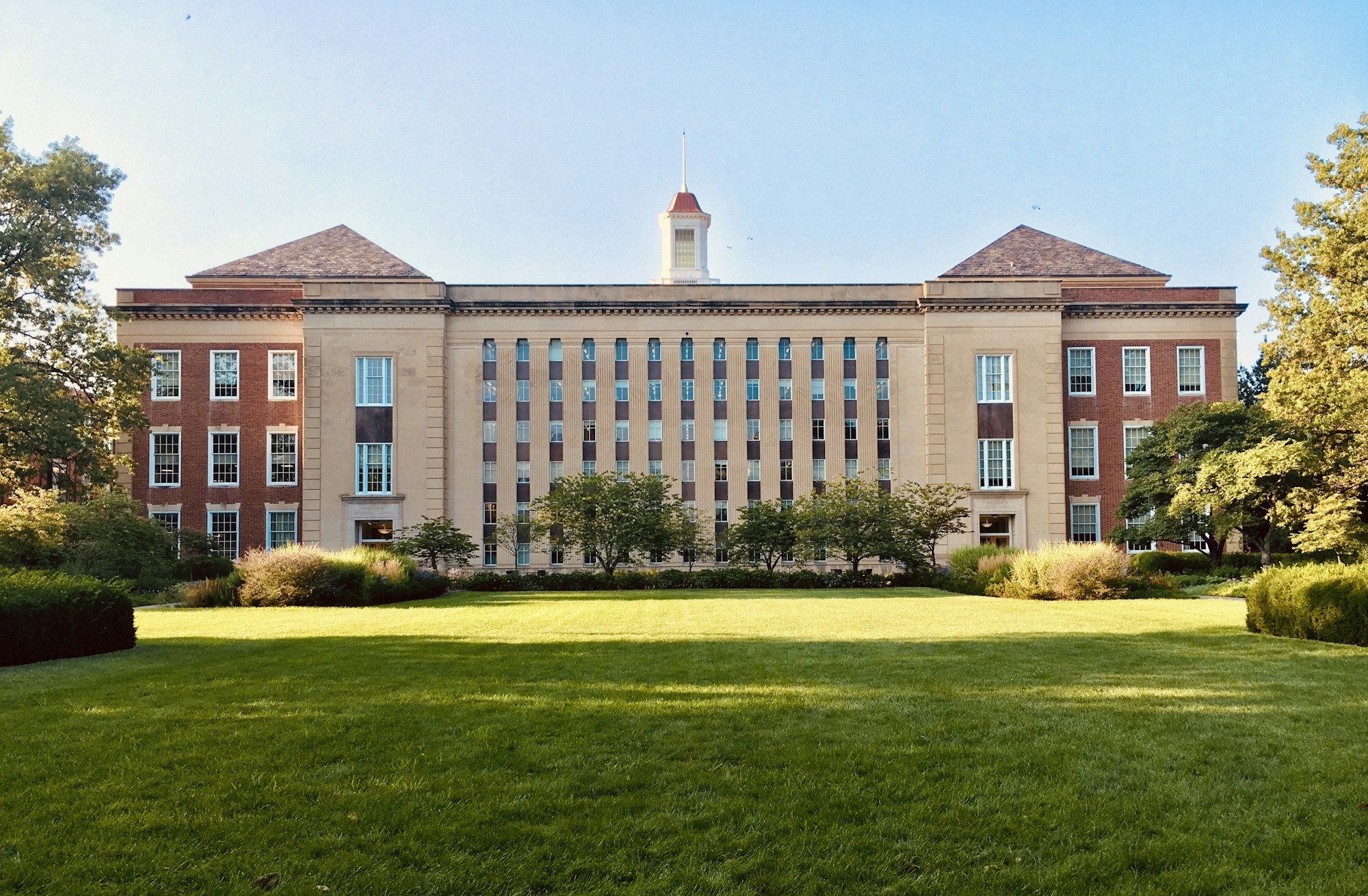 A red-brick academic building surrounded by trees and a green lawn